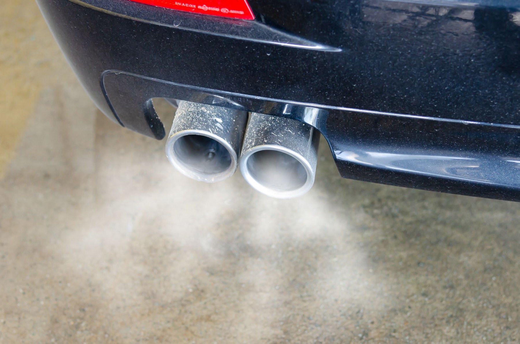 Close-up of a car's twin chrome exhaust pipes releasing smoke onto a concrete floor