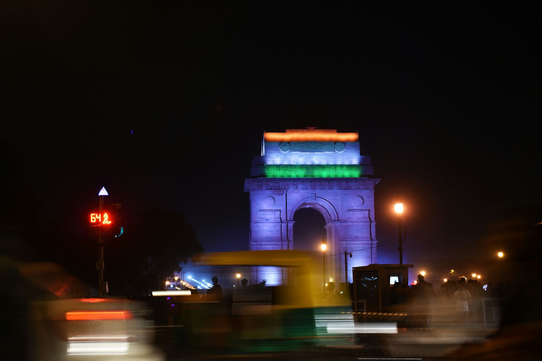 India Gate lit at night in New Delhi, with blurred auto-rickshaws in the foreground.